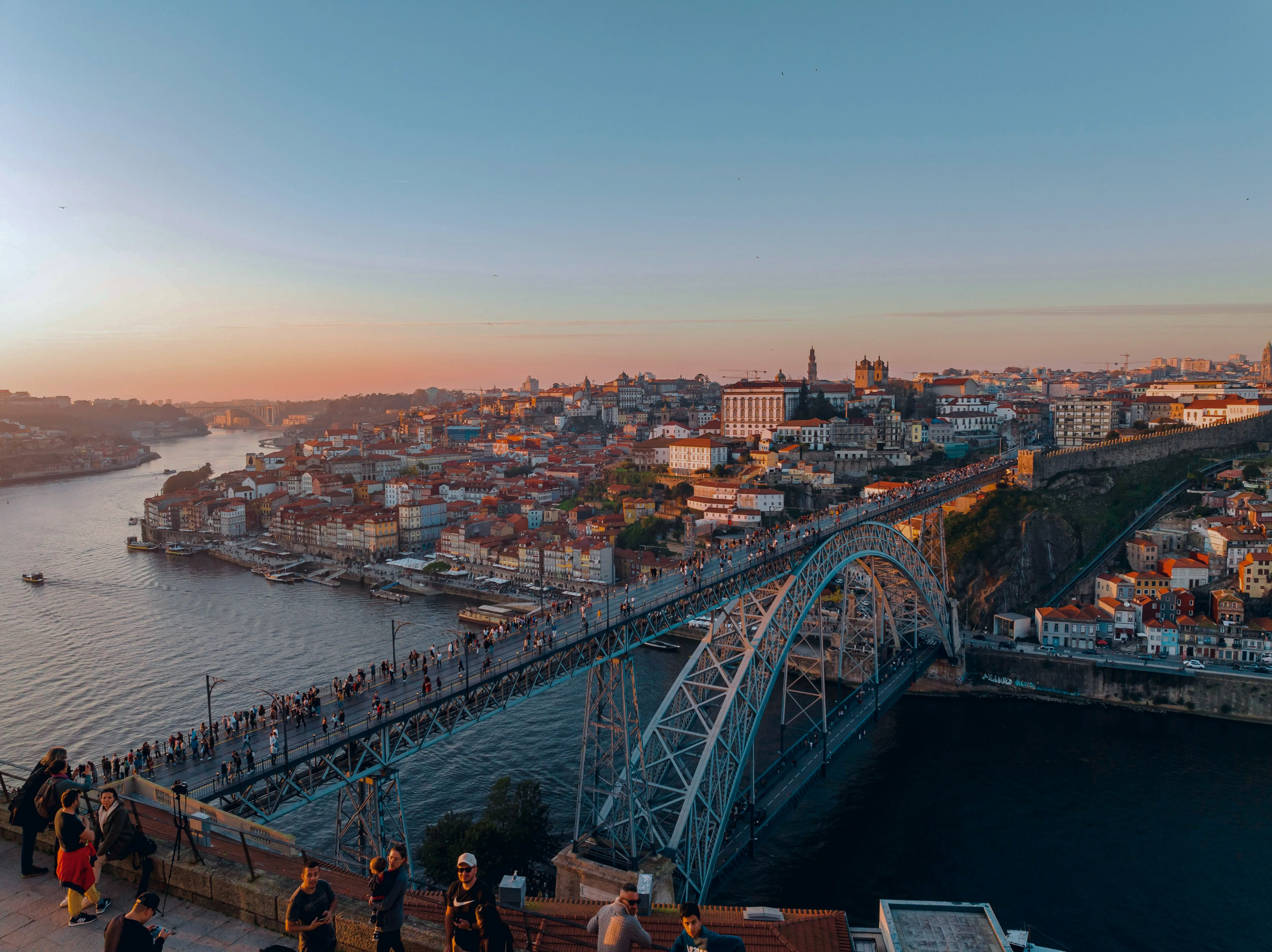 Dom Luís I Bridge in Porto at sunset, with city skyline in the background.